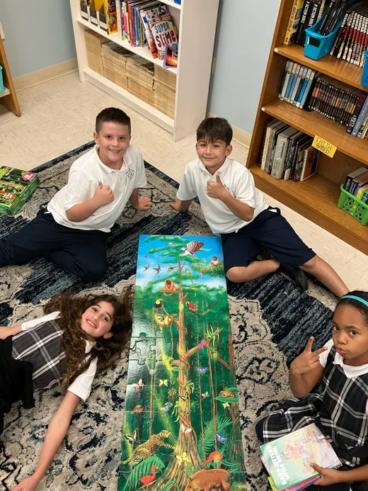 Students with a completed rainforest floor puzzle in the school library